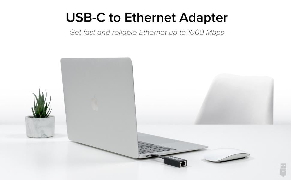 A laptop on a table with the USBC-TE1000 adapter plugged into it. There is a wireless mouse, a chair, and a decorative plant.